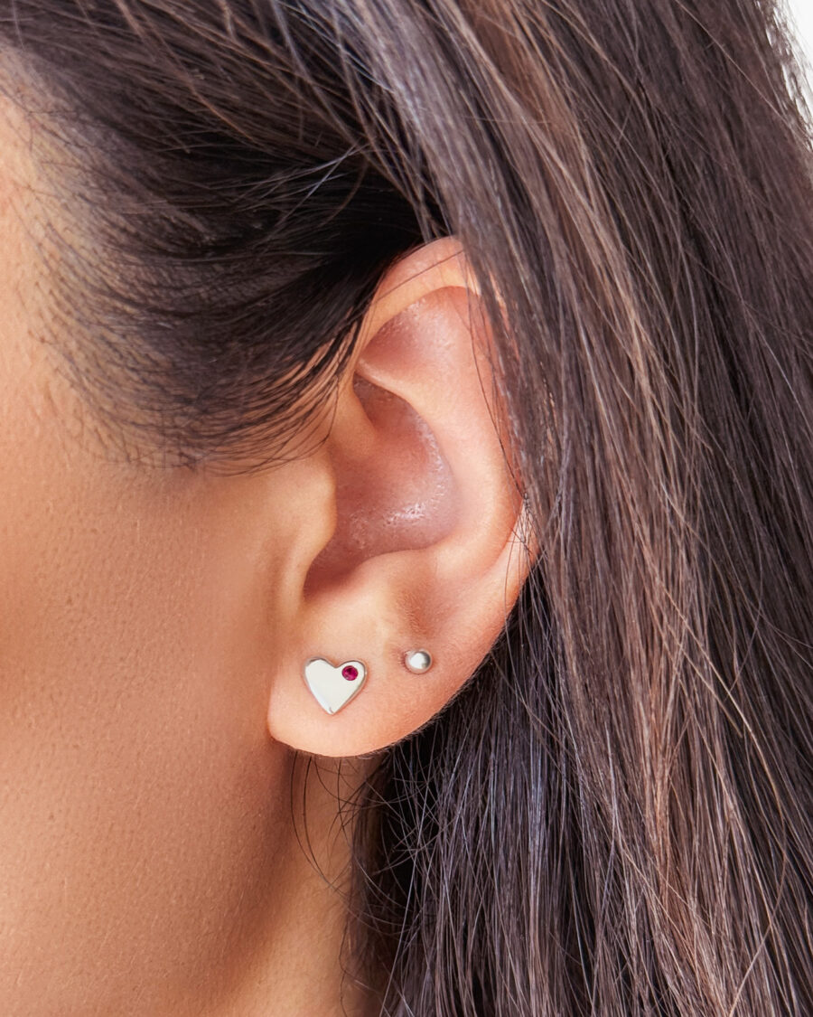 Oreja con un arete de corazón y un arete de bolita, ambos de plata 925